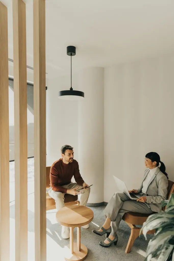 Two professionals engage in a thoughtful discussion in a stylish office setting, exchanging ideas while seated comfortably in contemporary chairs.